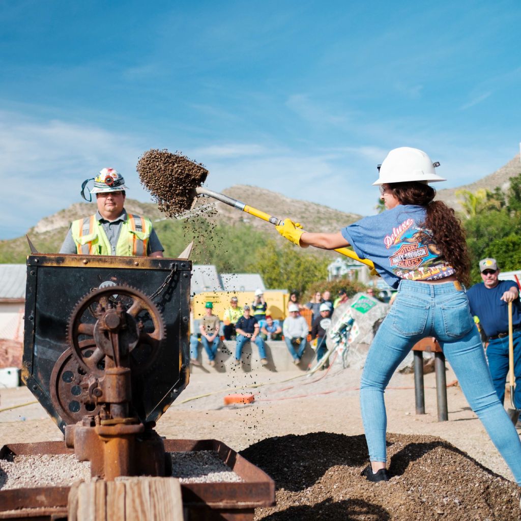 A woman in a hard hat is shoveling dirt with a shovel in Superior, AZ.